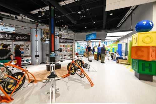 A vibrant indoor space featuring interactive exhibits, bicycles, and colorful blocks, with people exploring and engaging.