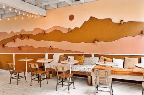 Cozy café interior with a warm color palette, featuring mountain murals, potted plants, and wooden seating.