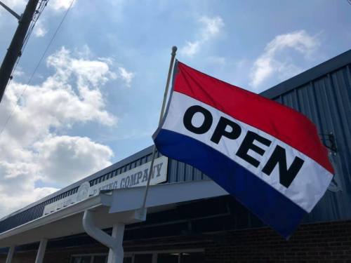 A red, white, and blue flag with "OPEN" displayed outside a building under a partly cloudy sky.