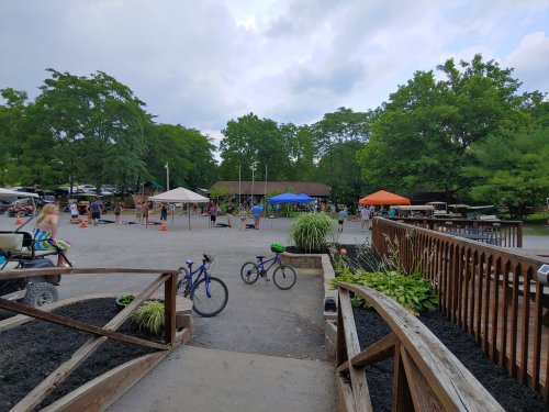 A view of a recreational area with tents, people, and bicycles, surrounded by trees and a cloudy sky.