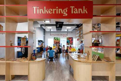 A colorful children's activity space with wooden tables, creative materials, and a sign reading "Tinkering Tank."