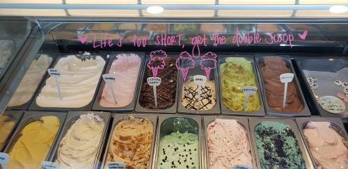 A display of various ice cream flavors in tubs, with a playful sign saying, "Life's too short, get the double scoop."