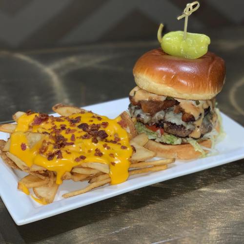 A juicy burger with cheese, lettuce, and a pepper on a bun, served with crispy fries topped with melted cheese and bacon bits.