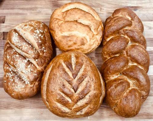 Four freshly baked loaves of bread on a wooden surface, featuring different shapes and textures.
