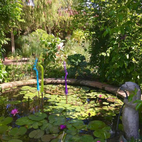 A serene garden pond with colorful glass sculptures, lily pads, and blooming water lilies surrounded by lush greenery.