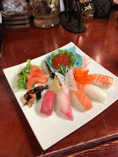 A beautifully arranged sushi platter featuring various types of sushi, sashimi, and garnishes on a white plate.
