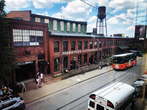 View of a historic brick building labeled "Marathon Automobiles" with a bus and people outside on a sunny day.
