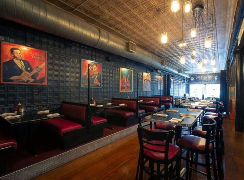Interior of a restaurant featuring red booths, wooden floors, and colorful artwork on the walls, with hanging lights.