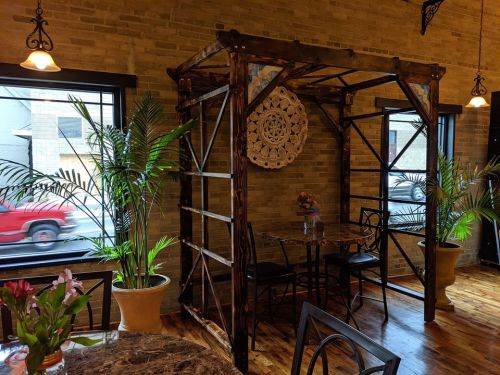 A cozy restaurant interior featuring a wooden structure, plants, and a table set near large windows.