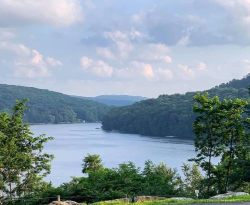 A serene view of a lake surrounded by lush green hills under a partly cloudy sky.