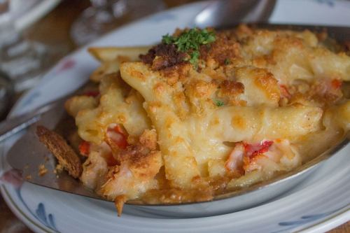A close-up of baked macaroni and cheese topped with breadcrumbs and herbs, served in a silver dish.