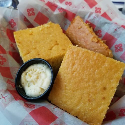 A basket with three pieces of cornbread and a small cup of butter.