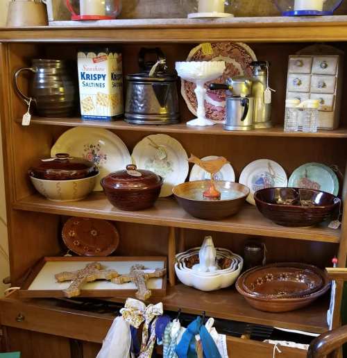 A wooden shelf displays various vintage items, including bowls, plates, and a can of saltines.