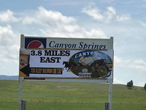 Sign for Canyon Springs, indicating it's 3.8 miles east, with a mention of Ten Sleep Brewing on tap.