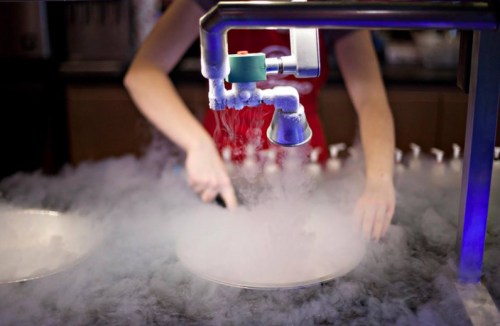 A person’s hands work with a machine creating smoke, likely using liquid nitrogen, over a round plate.