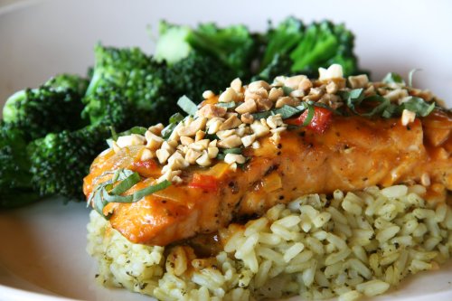 A plate featuring salmon on a bed of rice, topped with peanuts and herbs, alongside steamed broccoli.