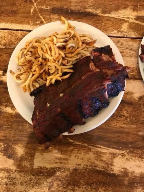 A plate of barbecue ribs next to a serving of curly fries on a wooden table.