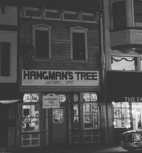 Historic building at night with a sign reading "Hangman's Tree" and a nearby street sign.