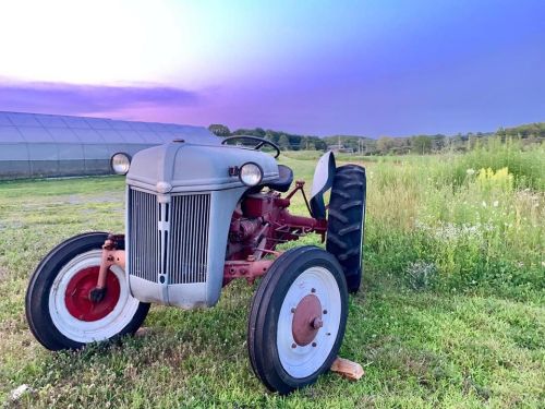 A vintage tractor parked in a grassy field with a colorful sunset in the background.