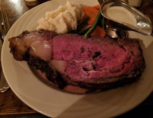 A plate of prime rib with mashed potatoes, carrots, green beans, and a side of gravy.