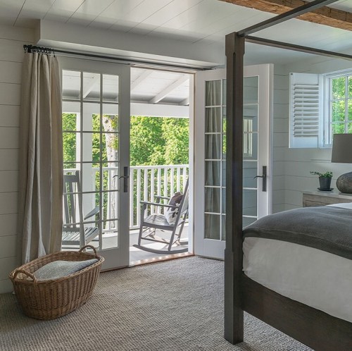 Bright bedroom with a four-poster bed, open French doors leading to a balcony, and a cozy wicker basket.