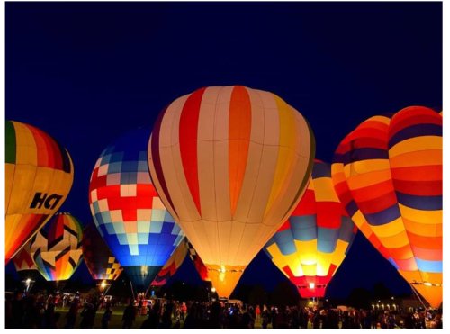 Colorful hot air balloons illuminated at night, surrounded by a crowd, creating a festive atmosphere.
