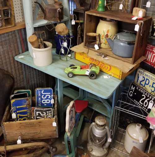 A vintage display featuring a blue table with various antiques, including kitchenware, toys, and old license plates.