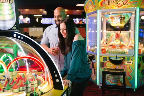 A couple enjoys playing a colorful arcade game in a lively gaming venue, smiling and having fun together.