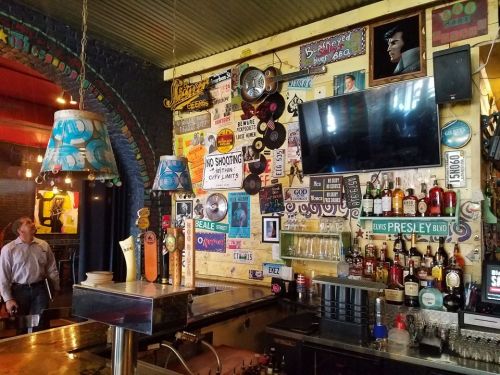 A vibrant bar interior featuring colorful wall decor, vintage signs, and a well-stocked counter with drinks.