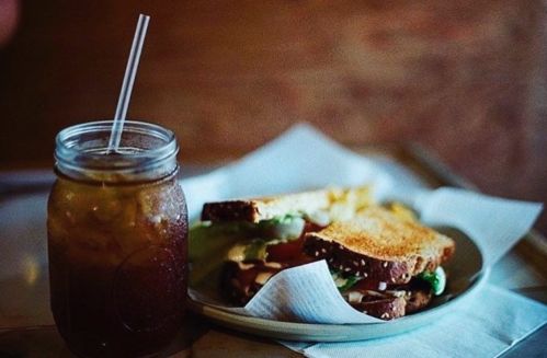 A mason jar of iced tea next to a plate of two toasted sandwiches on a napkin.