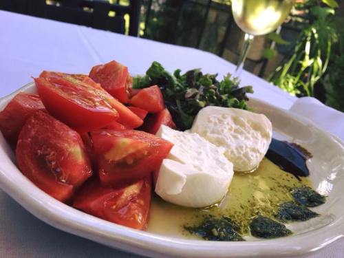 A plate of fresh tomatoes, mozzarella cheese, greens, and drizzled olive oil, with a glass of white wine in the background.