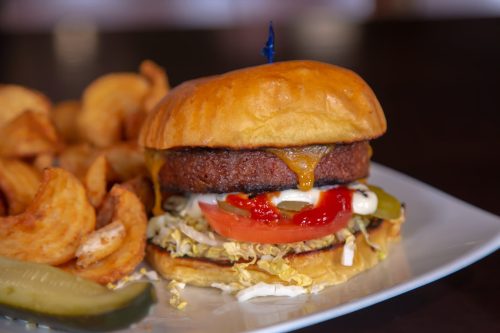 A juicy burger with cheese, lettuce, tomato, pickles, and condiments, served with crispy potato wedges on the side.