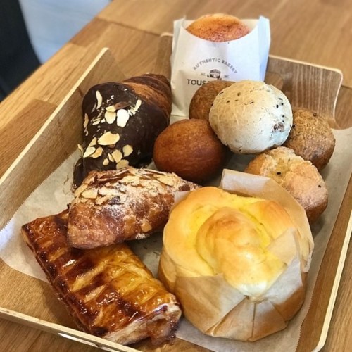 A wooden tray filled with various baked goods, including croissants, rolls, and pastries, arranged neatly.