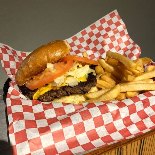 A juicy burger with lettuce, tomato, and cheese, served with a side of golden French fries in a checkered basket.