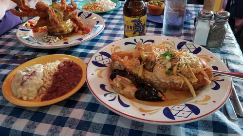 A colorful plate of seafood with rice, beans, and a drink, set on a checkered tablecloth.