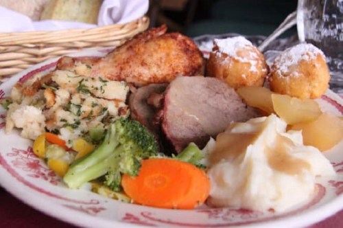 A plate of food featuring roasted chicken, pork, stuffing, mashed potatoes, broccoli, carrots, and dessert balls.