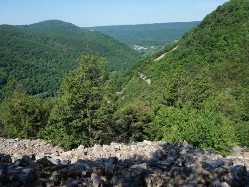 A scenic view of a lush green valley surrounded by mountains, with rocky terrain in the foreground.