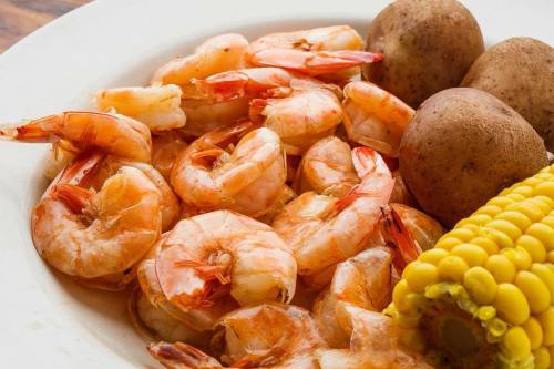 A plate of cooked shrimp, boiled potatoes, and corn on the cob.