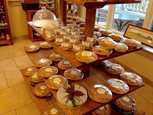 A wooden display shelf filled with various wrapped baked goods and pies, with a glass dome on top.