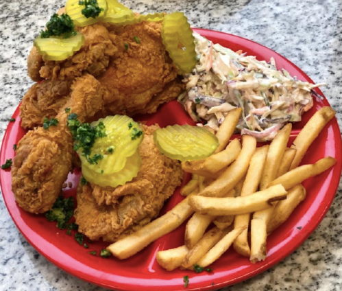 A red plate with crispy fried chicken, pickles, coleslaw, and golden French fries.