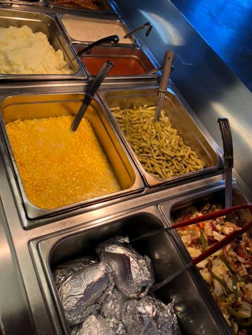 A buffet serving station with trays of mashed potatoes, corn, green beans, and baked potatoes.