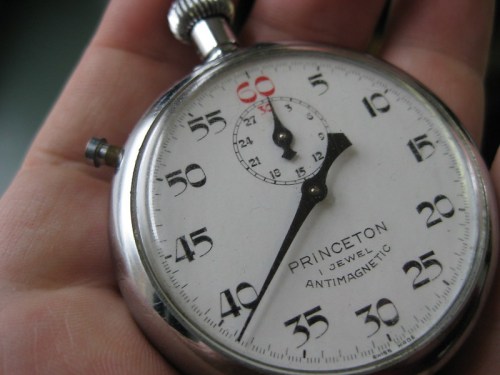 A close-up of a vintage Princeton stopwatch held in a hand, displaying seconds and minutes on a white face.