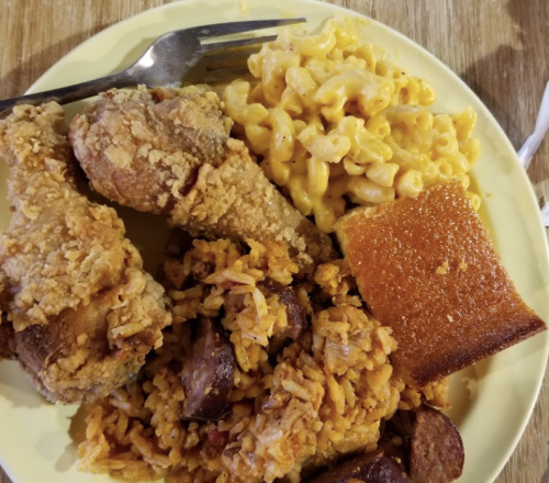 A plate of fried chicken, macaroni and cheese, sausage rice, and cornbread, served with a fork.