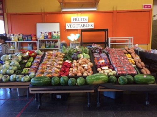 A vibrant market display featuring various fruits and vegetables, including watermelons, potatoes, and leafy greens.