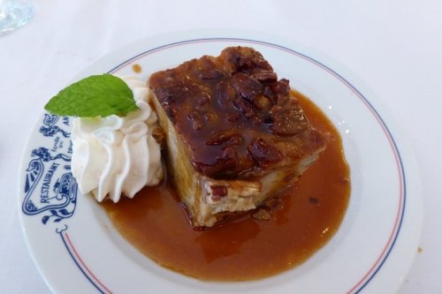 A slice of pecan pie topped with caramel sauce and a dollop of whipped cream, garnished with a mint leaf.