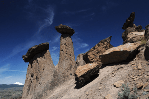 Unique rock formations with large, flat tops against a clear blue sky and distant mountains in the background.