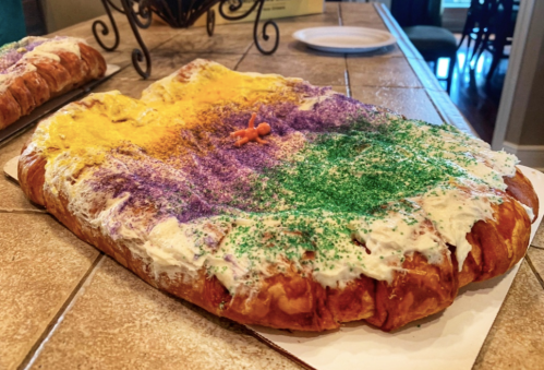A colorful king cake topped with yellow, purple, and green sprinkles, resting on a table.