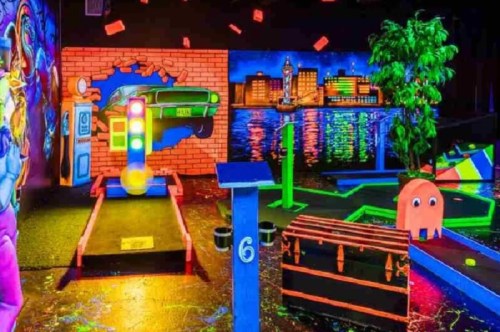 Colorful indoor mini-golf course with neon decorations, featuring a car mural and glowing obstacles.