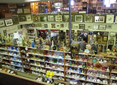 A bustling antique shop filled with shelves of collectibles, framed art, and various decorative items.