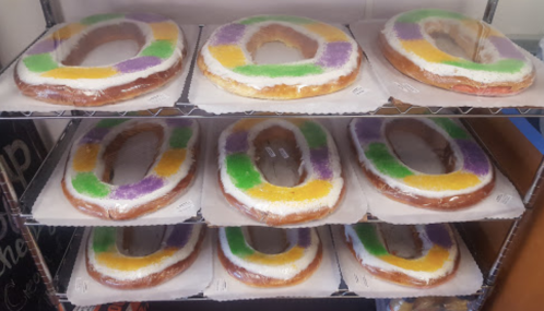 A display of large king cakes with colorful icing in purple, green, and yellow, arranged on a shelf.